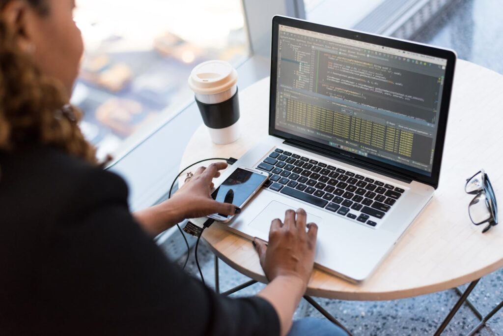 pexels-photo-1181243 Black woman programming on a laptop with coffee, smartphone, and glasses on a desk in an office.